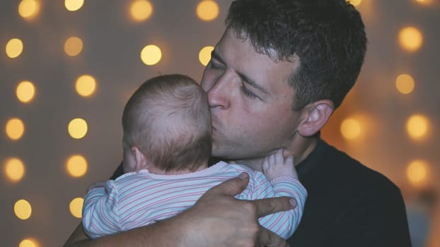 A father kisses his child in his arms at the evening lights