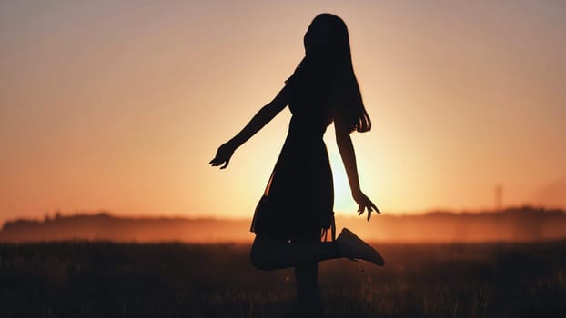 A silhouette of a young girl dancing and spinning on a warm summer evening at sunset