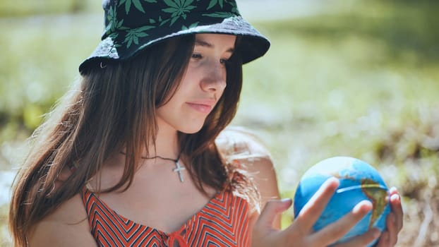 A teenage girl in a panama hat is looking at a globe of the earth