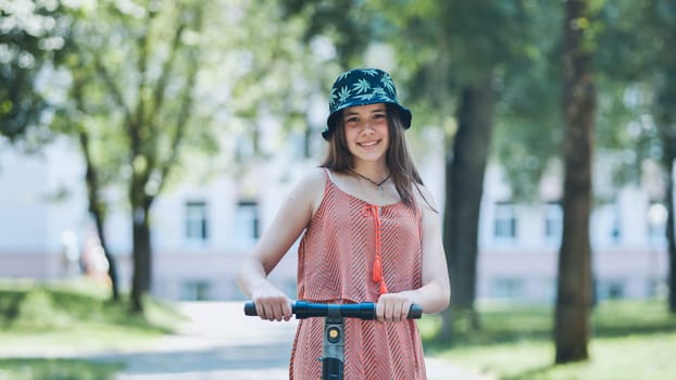 Portrait of a girl on an electric scooter posing in a park in the summer