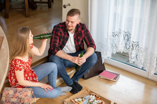 Learning together for the exam. A girl and a boy are sitting on the floor at home, with books lying next to them. The young people took a break and are drinking beer.