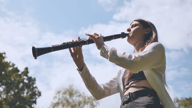 Girl plays clarinet against sky