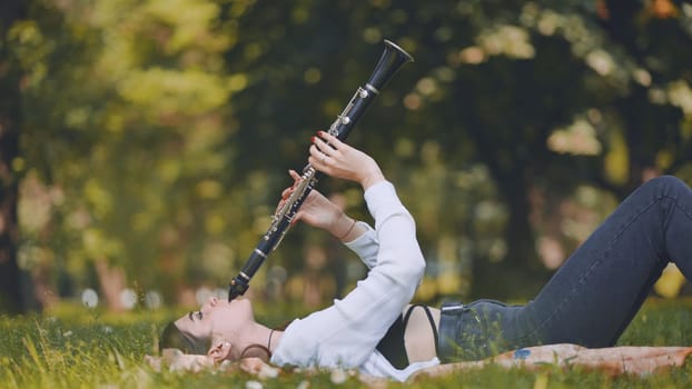 A girl plays the clarinet while lying on the grass in the park