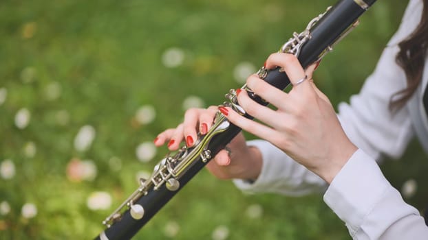 A girl plays the clarinet in the summer in the park. Close-up of her hands