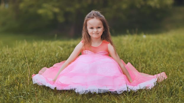 A little girl is sitting in a pink dress in the park