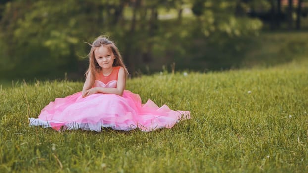 A little girl is sitting in a pink dress in the park