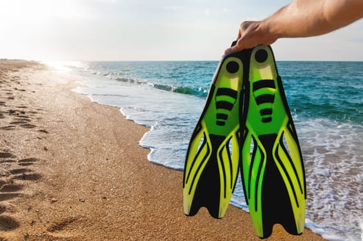 a man holds flippers in his hands, against the backdrop of the sea coast. Summer sea holiday in wilderness area for snorkeling