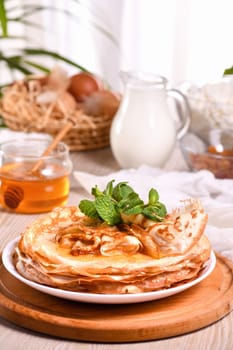 Homemade thin crepe (pancakes) with honey stacked in a stack, on a table with milk and eggs in a basket. Country style food. Traditional Slavonian, pagan holiday Maslenitsa