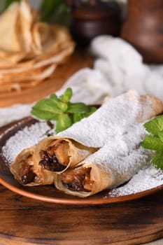 Homemade thin pancakes. The apples are cooked in a buttery caramel sauce with raisins and cinnamon and stuffed into a thin pancake. Garnish with powdered sugar and mint. Food in a rustic style.