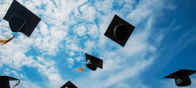 Silhouetted graduation caps thrown aloft against a sunny blue sky with sun rays and clouds