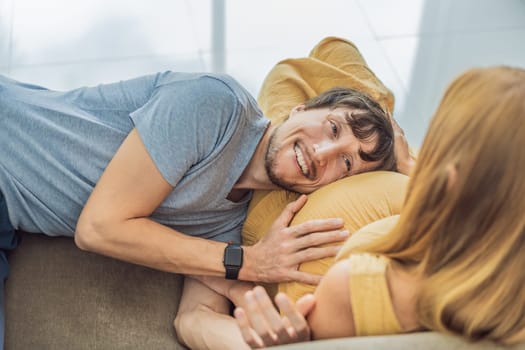 Tender moment as husband lovingly embraces his pregnant wife's belly while they lie together on the sofa, sharing warmth and anticipation.