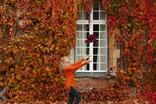 Woman in an orange sweater near a wall with wild grapes in autumn