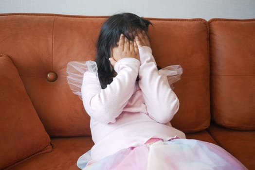 a upset child girl cover her face with hand .