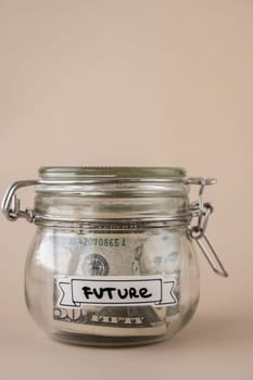 Saving Money In Glass Jar filled with Dollars banknotes. FUTURE transcription in front of jar. Managing personal finances extra income for future insecurity. Beige background