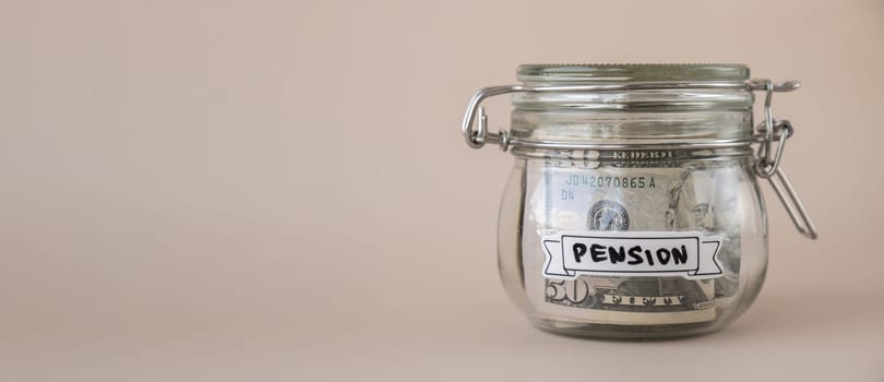 Saving Money In Glass Jar filled with Dollars banknotes. PENSION transcription in front of jar. Managing personal finances extra income for future insecurity. Beige background