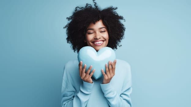 Beautiful African American woman holding and hugging big blue heart on blue background. St Valentine's Day vibe
