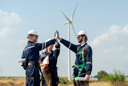 Group of professional technician workers men and woman stand with touch hands in front of roll of wind turbine or windmill in the field area of power plant business.
