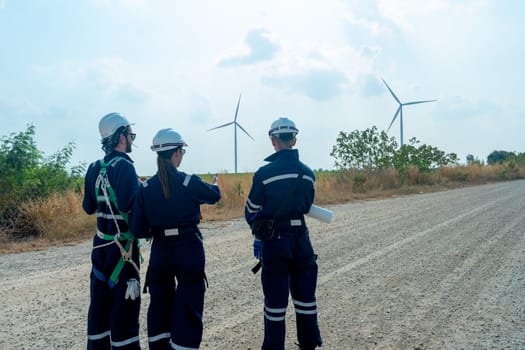 Close up back of group of technician workers stand on the road and discuss about work with windmill or wind turbine on the background.