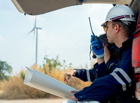 Technician worker man use walkie talkie to contact his co-worker and sit in the back of van in area of power plant with wind tubine or windmill.