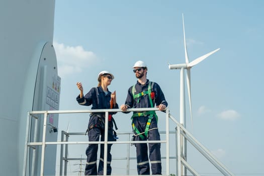 Professional workers stand and discuss about work and stay in base of windmill or wind turbine in area of green power plant.