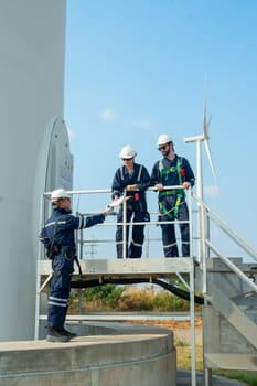 Vertical image professional technican worker give the document to his coworkers stand in base of windmill or wind turbine also discuss about work.