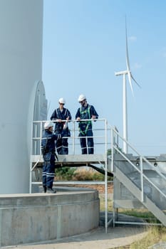 Vertical image one technican worker give the document to his coworker stand in base of windmill or wind turbine.