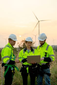 Vertical image group of technician workers man and woman work using laptop and stay in front of windmill or wind turbine with evening light.