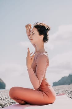 Young woman with long hair in white swimsuit and boho style braclets practicing outdoors on yoga mat by the sea on a sunset. Women's yoga fitness routine. Healthy lifestyle, harmony and meditation