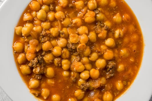 Chickpea stew with minced meat on a white porcelain plate on a stone table