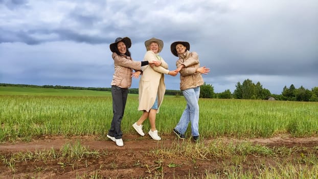 Adult girls looking like a cowboys in hats in a field and with a stormy sky with clouds posing in the rain. Women having fun outdoors on rural and rustic nature