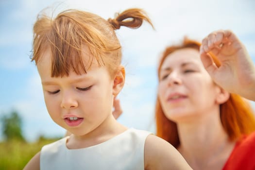 Happy female family with mother and daughter on green and yellow meadow full of grass and flower. Woman with red hair and blonde girl having fun, joy and hug in sunny summer day. Concept family love