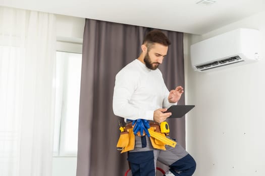 Young Technician using digital tablet and pen checking air conditioner in house room. Air Conditioning system installation and repairing concept.