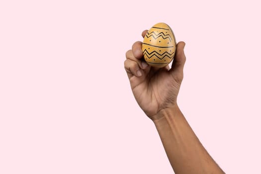 Male hand holding modern painted easter egg on pink background. High quality photo