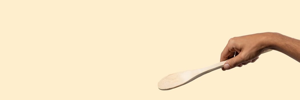 Male hand holding wooden spoon on light beige background. High quality photo