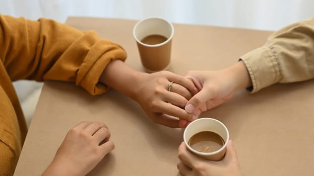 Top view of married couple holding hands and drinking coffee in coffee shop.