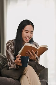 Relaxed young woman in casual clothes reading book, spending free time at home on weekend.