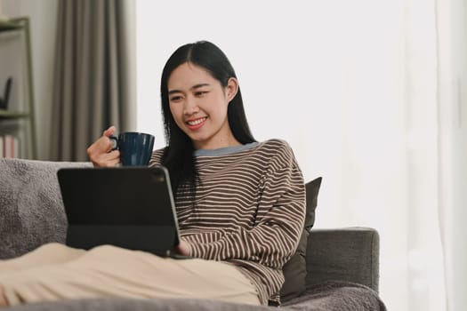 Carefree young Asian woman watching video on digital tablet. People, technology and lifestyle.