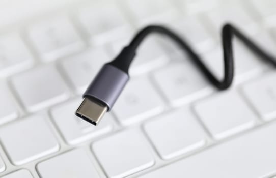 Close up, on computer keyboard cord with adapter. Usb input for tablet lies on keyboard. Self-training on computer and accessories. External sound card for laptop. Wire to connect to device