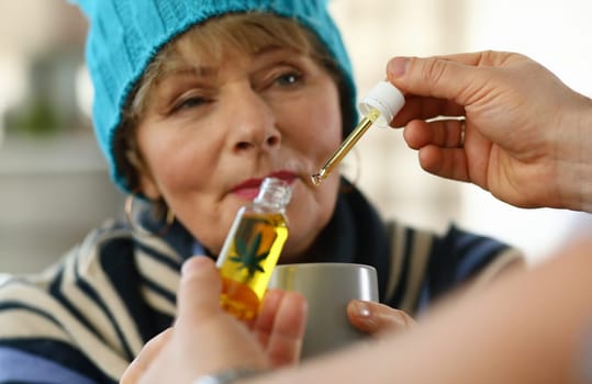 Sick elderly woman at home takes drops cannabis cup. Side effects drugs. Cold medicine for elderly. Weak immune system in old age. Use the drug in therapeutic doses. Danger to elderly
