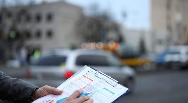 Man on street fills out an accident statement. Filling in by driver for subsequent transfer this information to insurance company. Accident reports on road. Keep calm during an accident on street