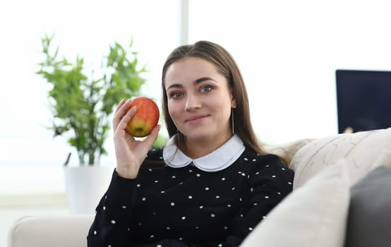 Girl sitting at home couch with apple in her hands. Girl does not work, but sits at home. Comfortable living while studying. Transition to healthy diet at young age. Social phobia and joy loneliness