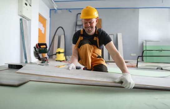 Happy carpenter places laminate panels on floor. Man gives instructions for laying substrate and laminate. Simplicity in installation floor material. Serial connection one board with another