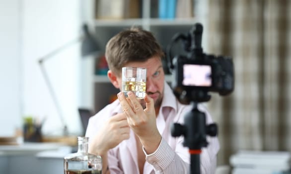 Drunk man looks glass alcohol and takes off camera. Guy drinks at home during quarantine. Video blogger tastes alcoholic drinks for subscribers. Falsification branded alcohol video