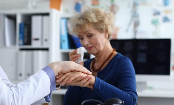 An elderly woman cries at doctor's appointment. Doctor helps an elderly woman resist during an illness. Reaction to the diagnosis of the doctor, the woman is crying. Patient after examination