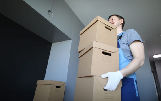 Male loader carries empty cardboard boxes indoors. Man in work clothes and gloves carries boxes. Folding drawers. Things are collected for moving. Collection goods in warehouse online store