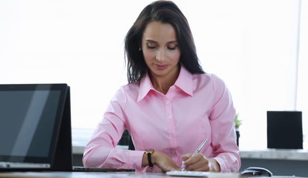 Girl makes notes with pen at table in office. Calculation attractiveness financial project. Financial literacy employee training. Woman fills out document in workplace. Equipped workplace in office