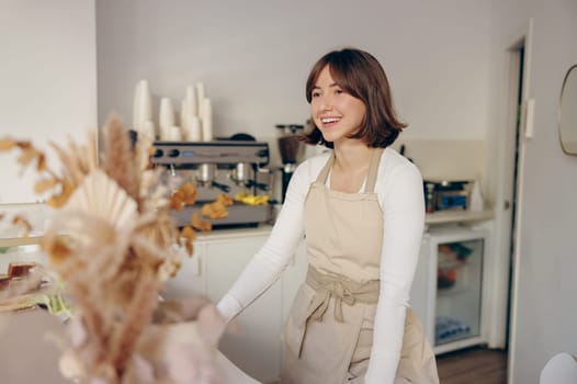 Beautiful female barista is looking away and smiling while standing near bar counter in cafe