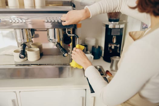 Close up of female barista cleaning coffee machine at coffee shop after froths milk . High quality photo