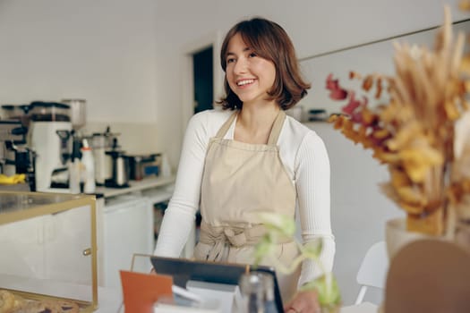 Portrait of a happy female barista standing behind the counter in a coffee shop