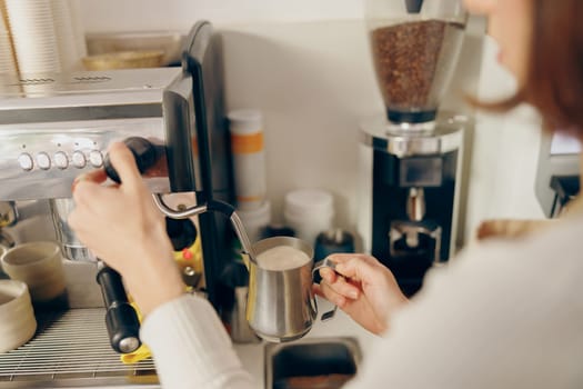 Close up of female barista frothing milk for coffee with professional coffeemaker working in cafe